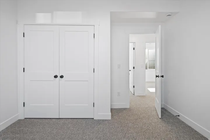 Double-panel closet doors featuring matte black hardware, crisp white trim, and light grey carpet flooring