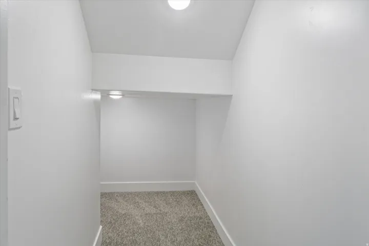 Recessed niche with a light fixture, light gray carpet flooring, white baseboards, and a wall-mounted light switch
