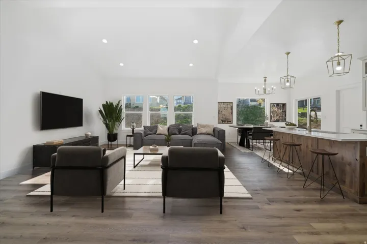 AI generated Expansive open-concept living area featuring high vaulted ceilings with recessed lighting, wood-finish flooring, a kitchen island with seating, and a dining area