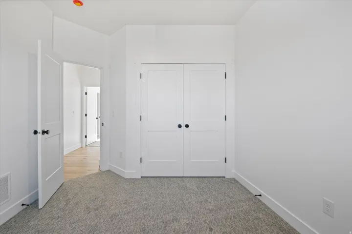 Carpeted room featuring white walls, a white bi-fold closet door with matte black hardware, and a white interior door with matte black hardware
