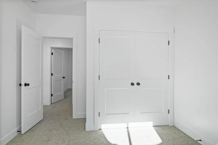 White paneled bi-fold doors with round black hardware complement the light-colored carpet flooring