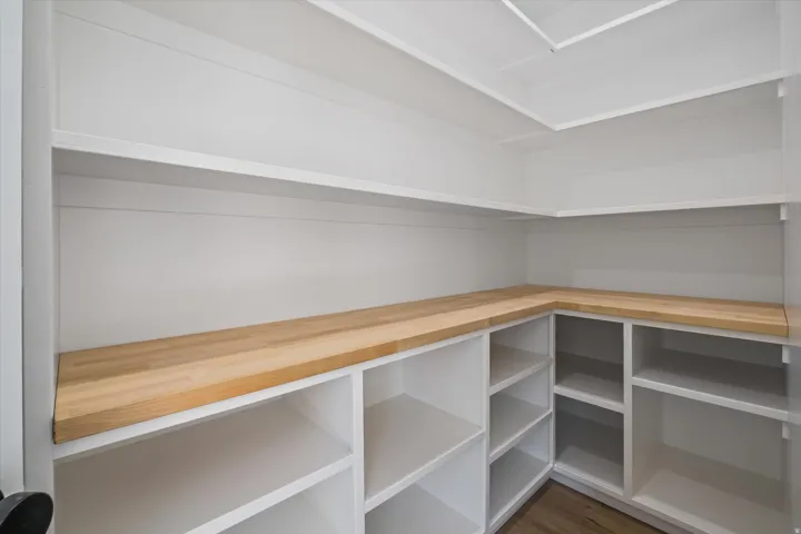 Spacious pantry featuring white built-in shelving, wood-finish countertops, and wood-finish flooring