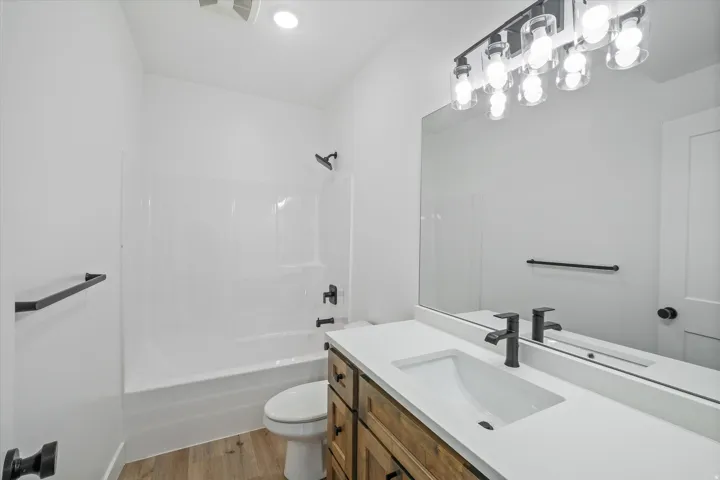 Full bathroom featuring a white tub/shower combination, dark bronze fixtures, wood-finish flooring, a wood-finish vanity with an integrated white sink, and an expansive wall mirror