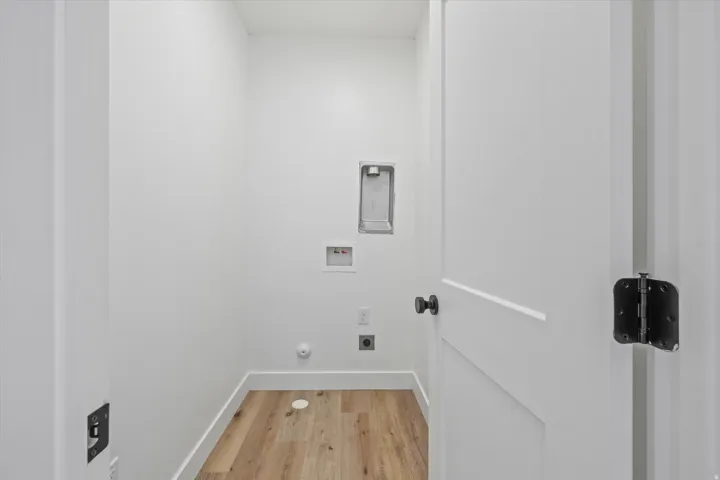 Dedicated laundry utility space with wood-finish flooring, crisp white walls, and a recessed dryer vent