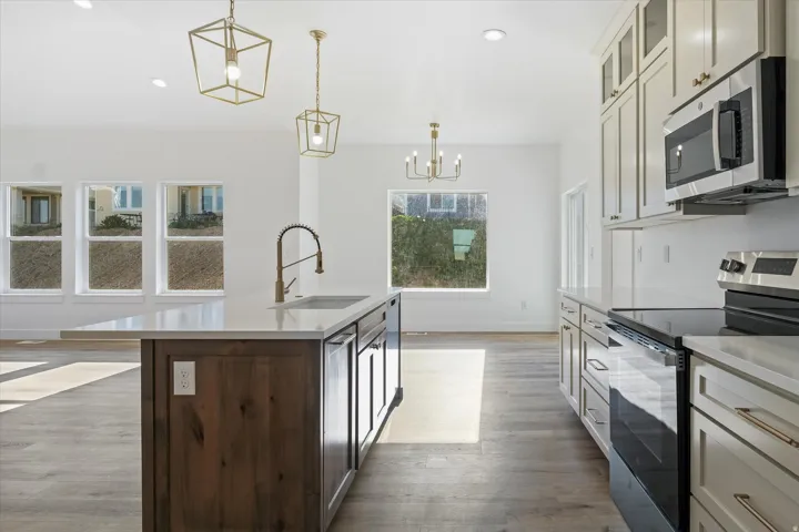 Contemporary kitchen featuring a large central island with a sink and wood-finish cabinetry, stainless steel appliances, white shaker-style perimeter cabinetry, light-toned countertops, and wood-finish flooring
