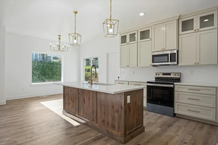 Open-concept kitchen featuring a wood-finish island with a white countertop, light-toned cabinetry with glass-front accents, and stainless steel appliances