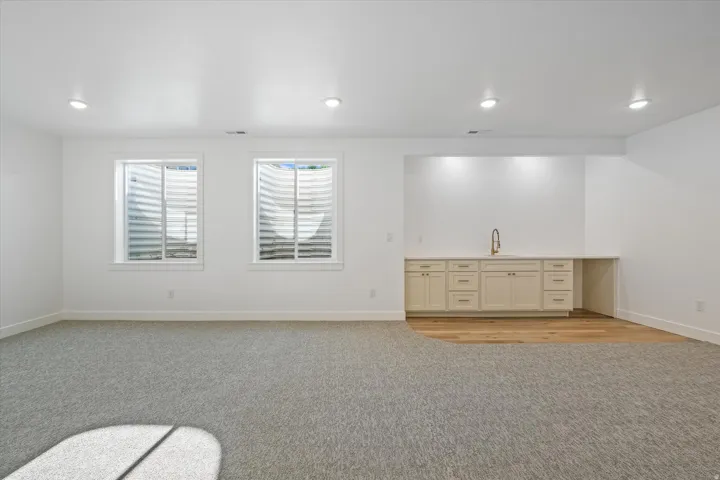 Lower-level living area featuring recessed lighting, two windows, and a built-in wet bar with cabinetry, a sink, and wood-finish flooring