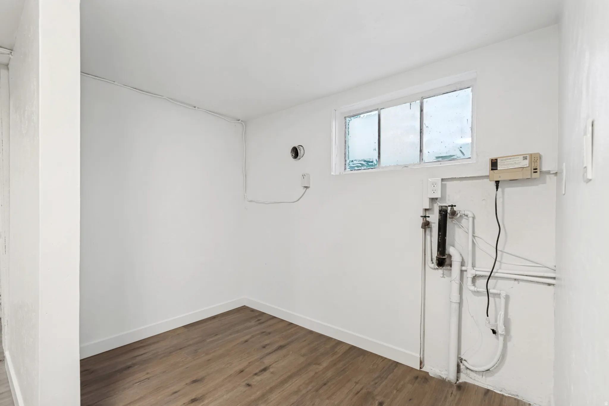 Room with wood-finish flooring, white walls, and a visible window