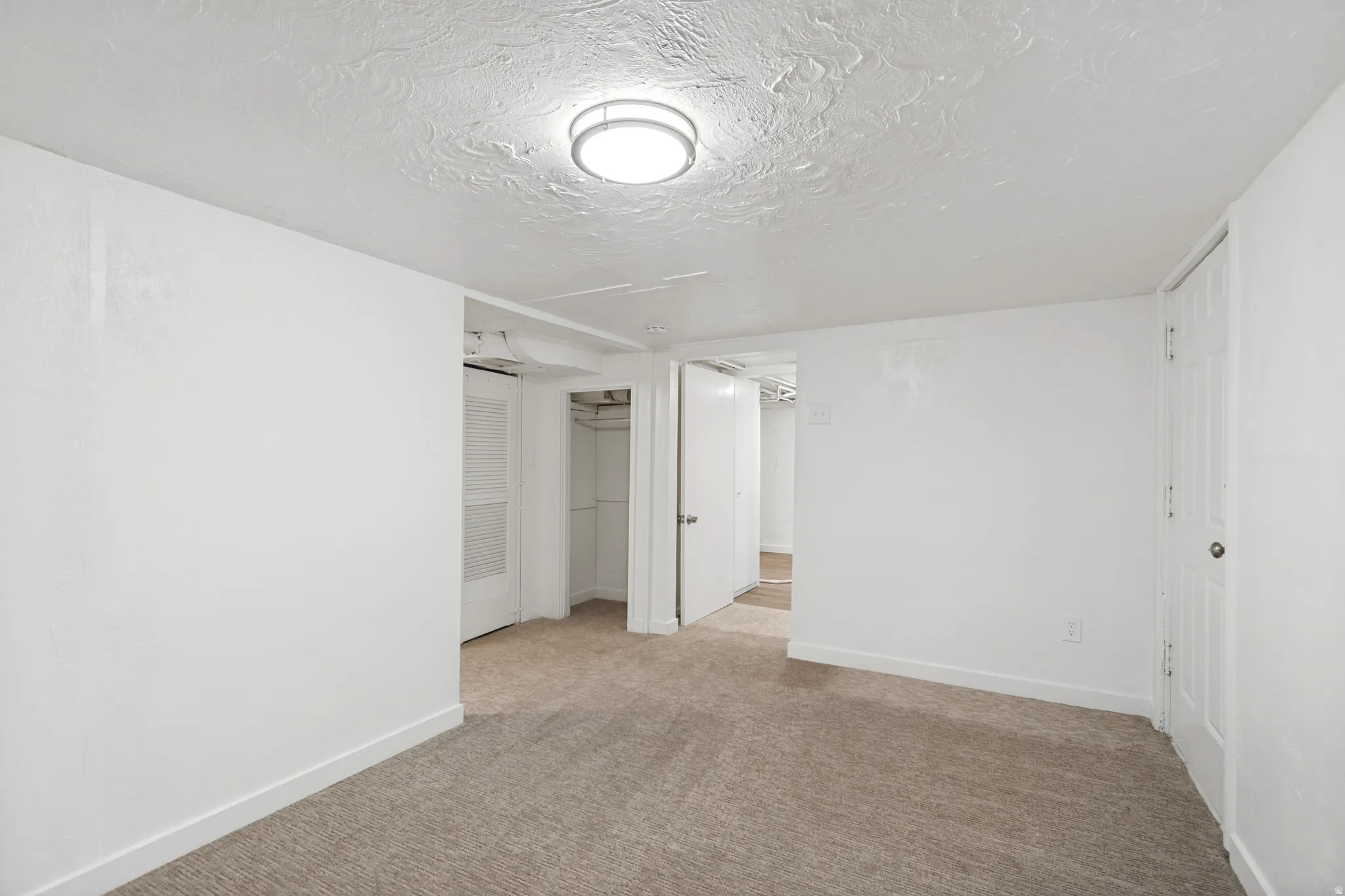Carpeted room featuring white walls, a textured ceiling, and a flush-mount ceiling light fixture