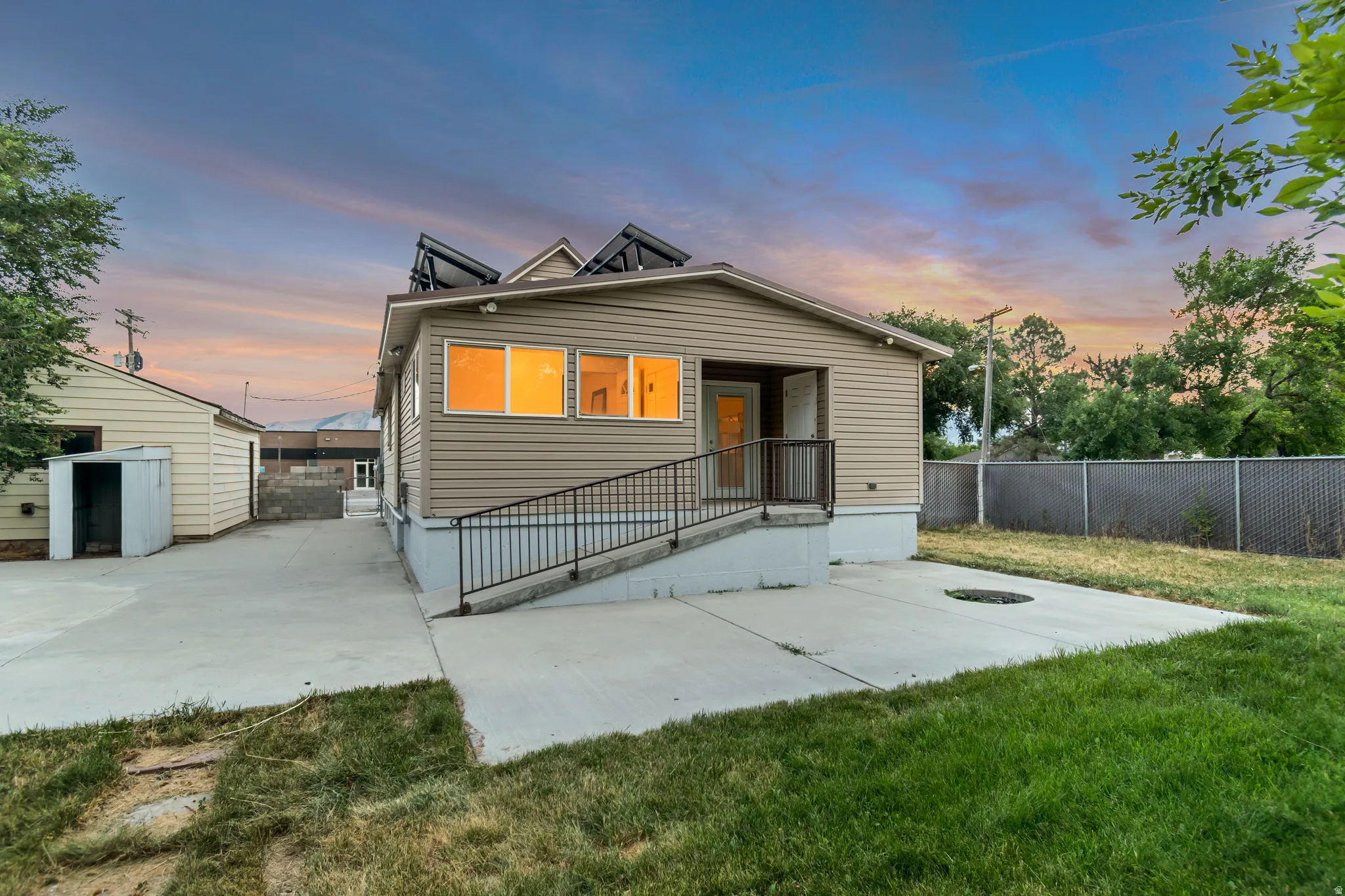 Rear exterior featuring beige siding, multiple windows, a concrete patio, and a ramp entry with handrails