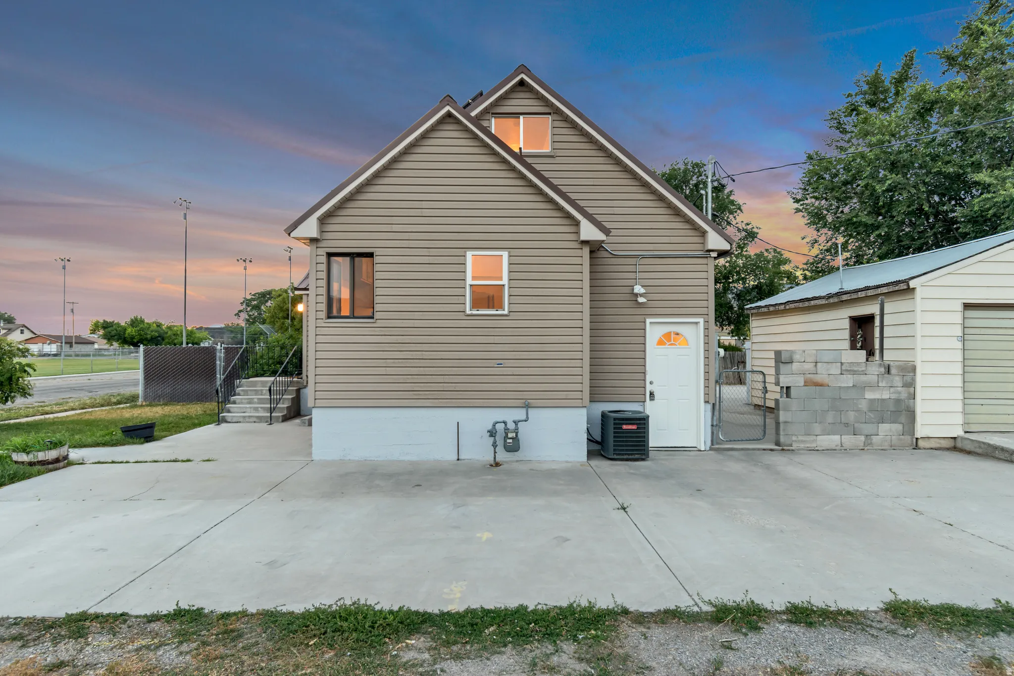 Rear exterior featuring tan siding, a white entry door with a decorative window, and a concrete driveway