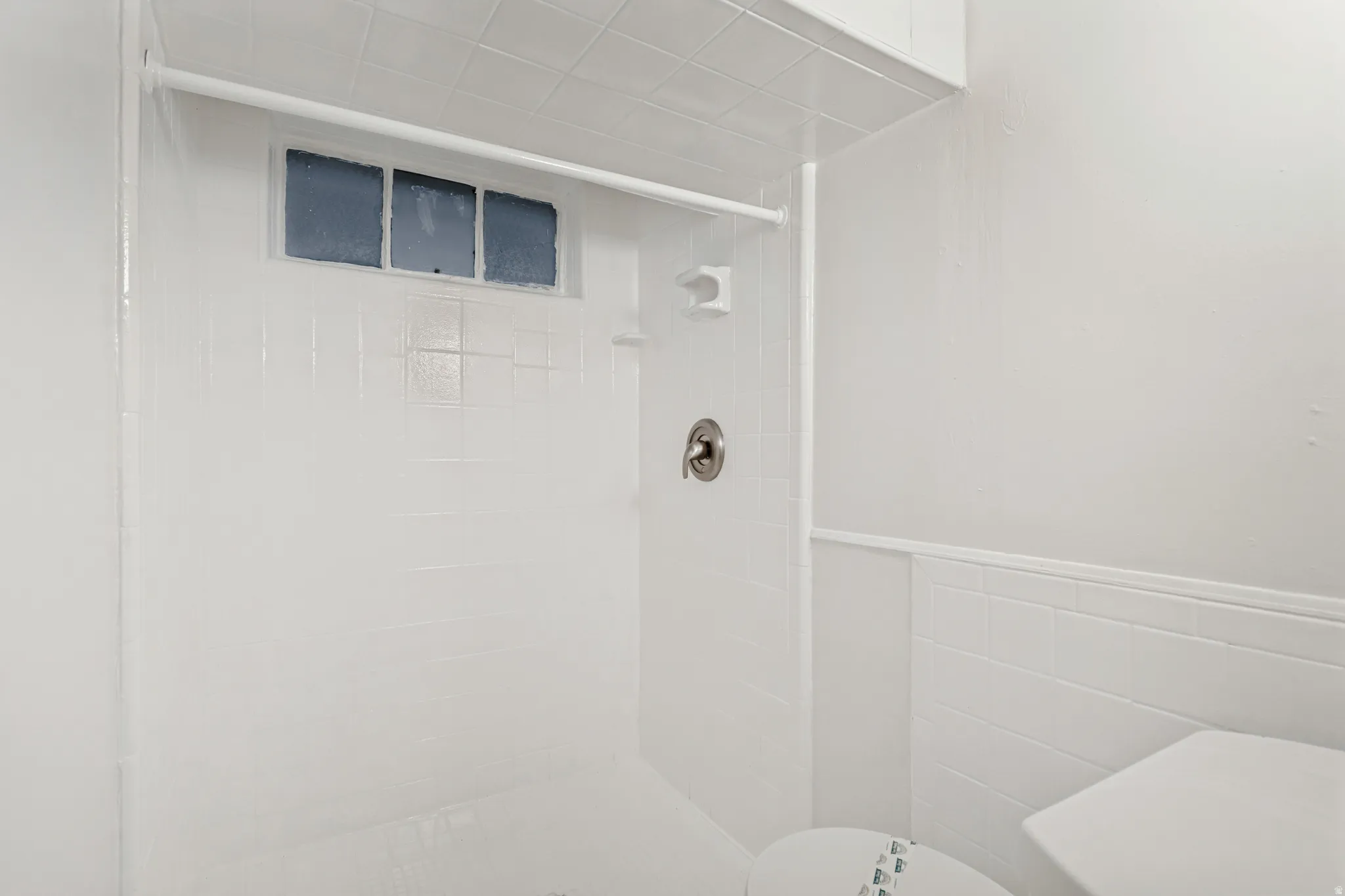 Bright white tiled shower enclosure featuring a satin nickel shower fixture, a privacy window, and a built-in shelf