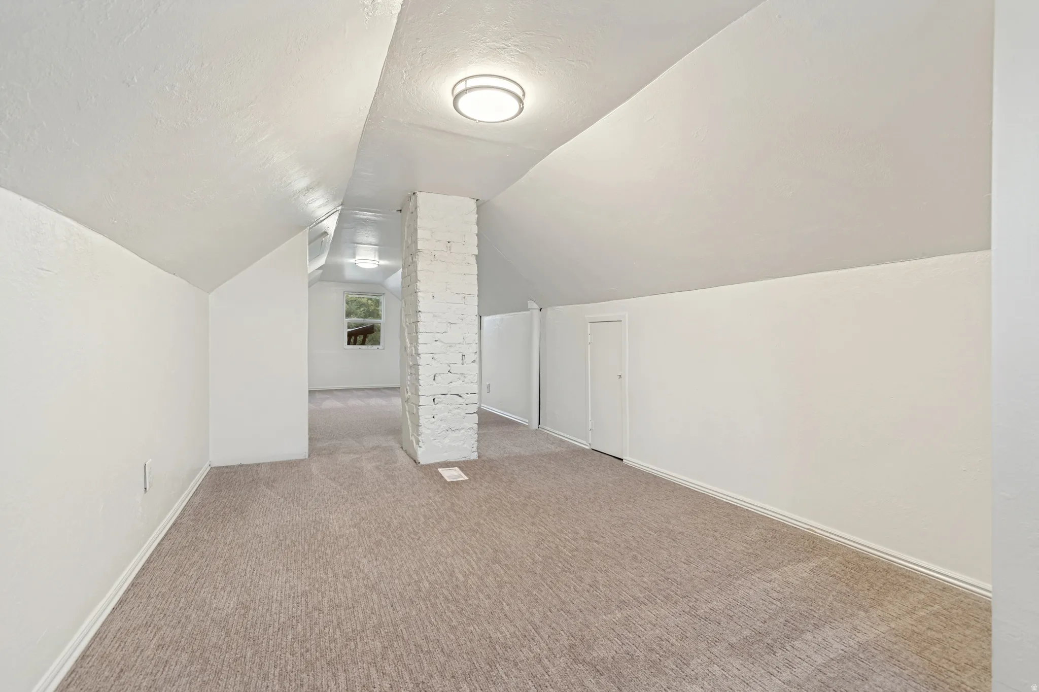 Carpeted room with a whitewashed brick column and sloped ceilings