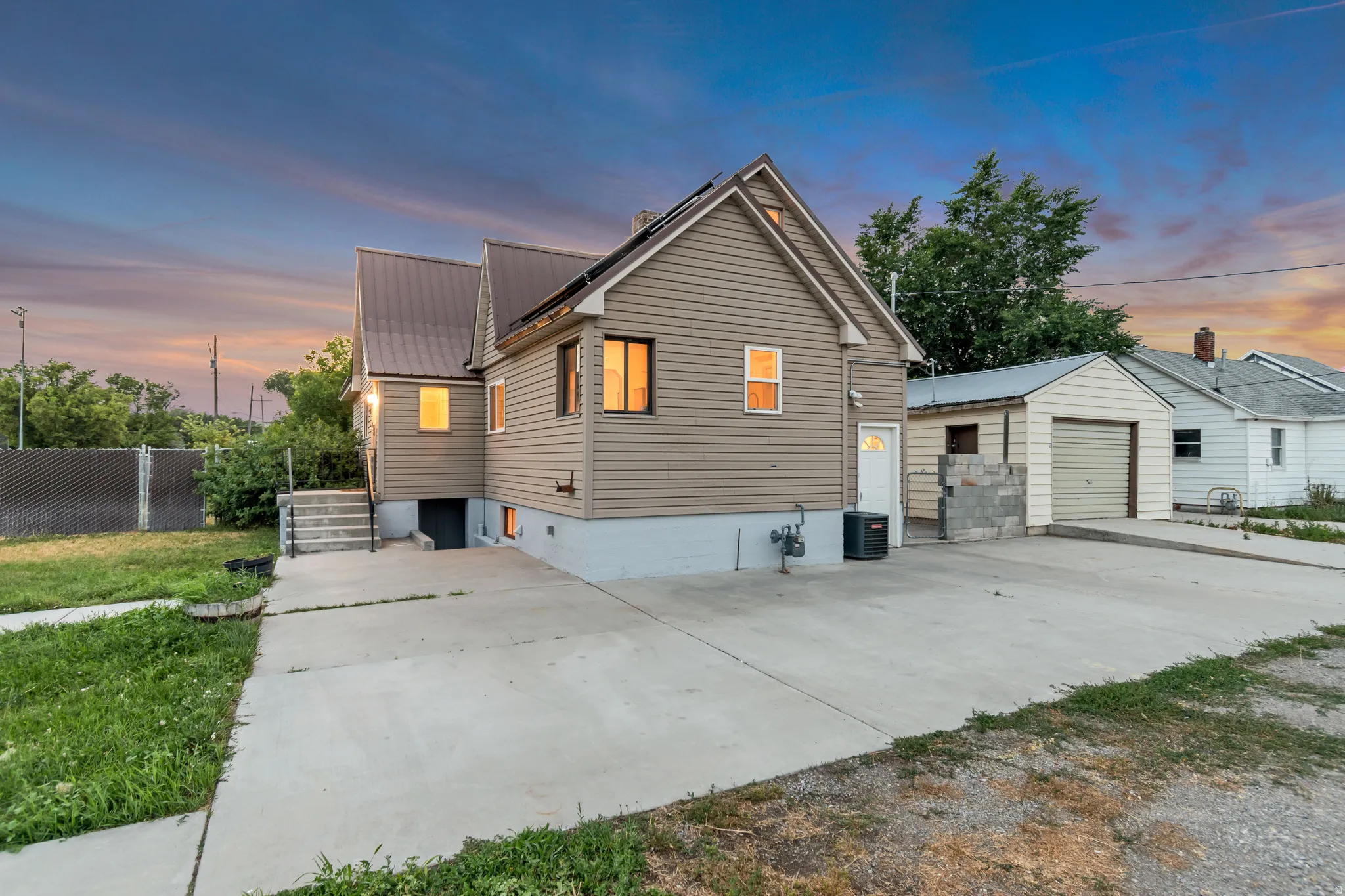 Exterior featuring beige siding, a metal roof, multiple windows, a concrete driveway, and a detached garage