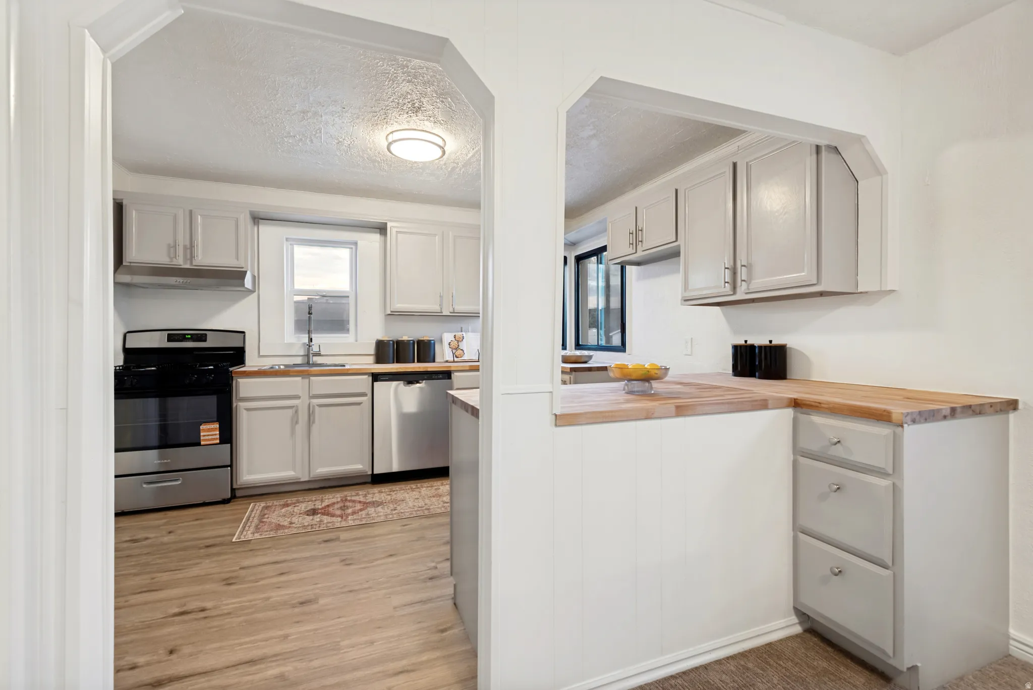 Kitchen featuring light gray cabinetry, wood-finish countertops, stainless steel appliances, and wood-finish flooring