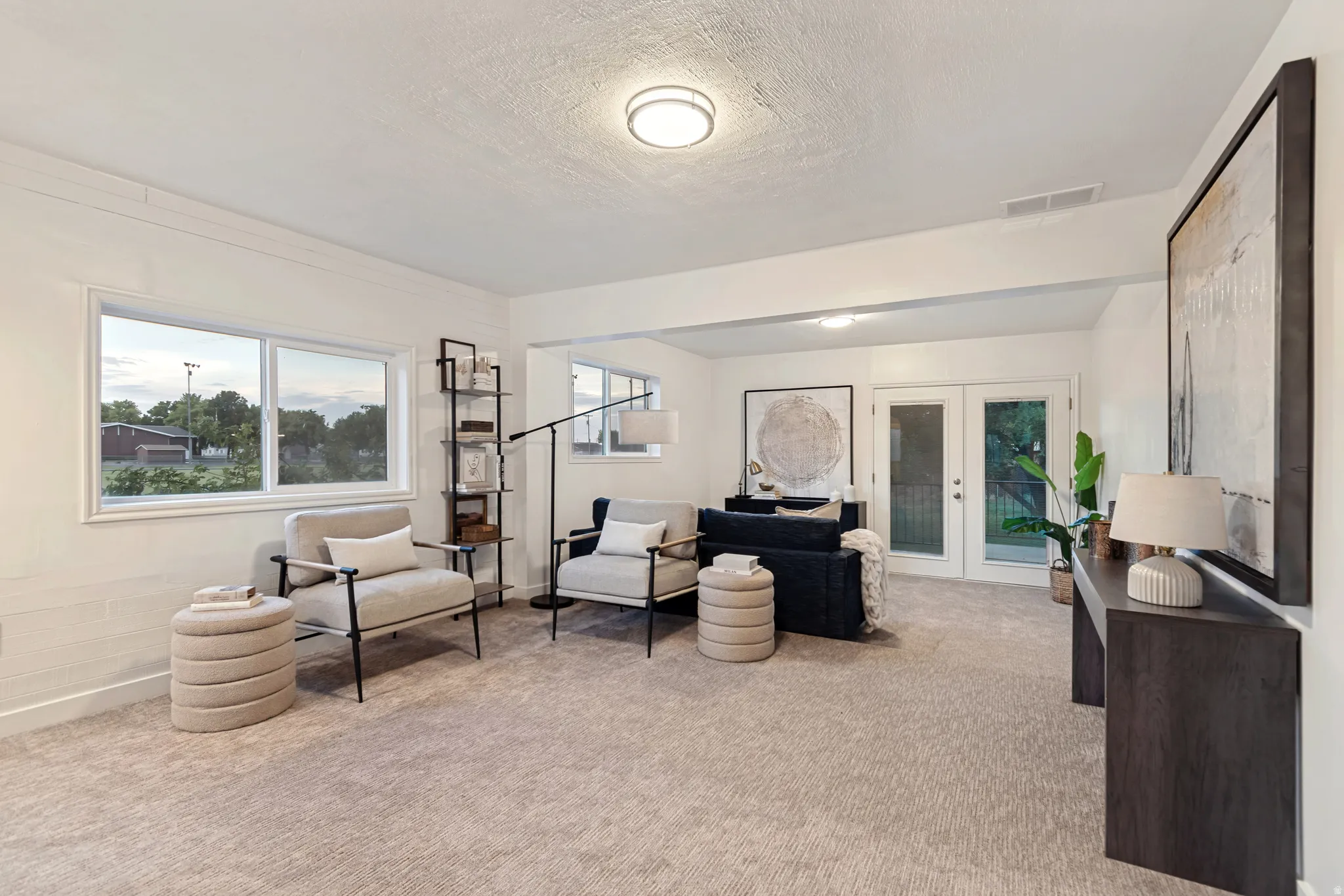 Recessed lighting illuminates this living area featuring neutral-toned carpeting, white walls, and a pair of sliding windows