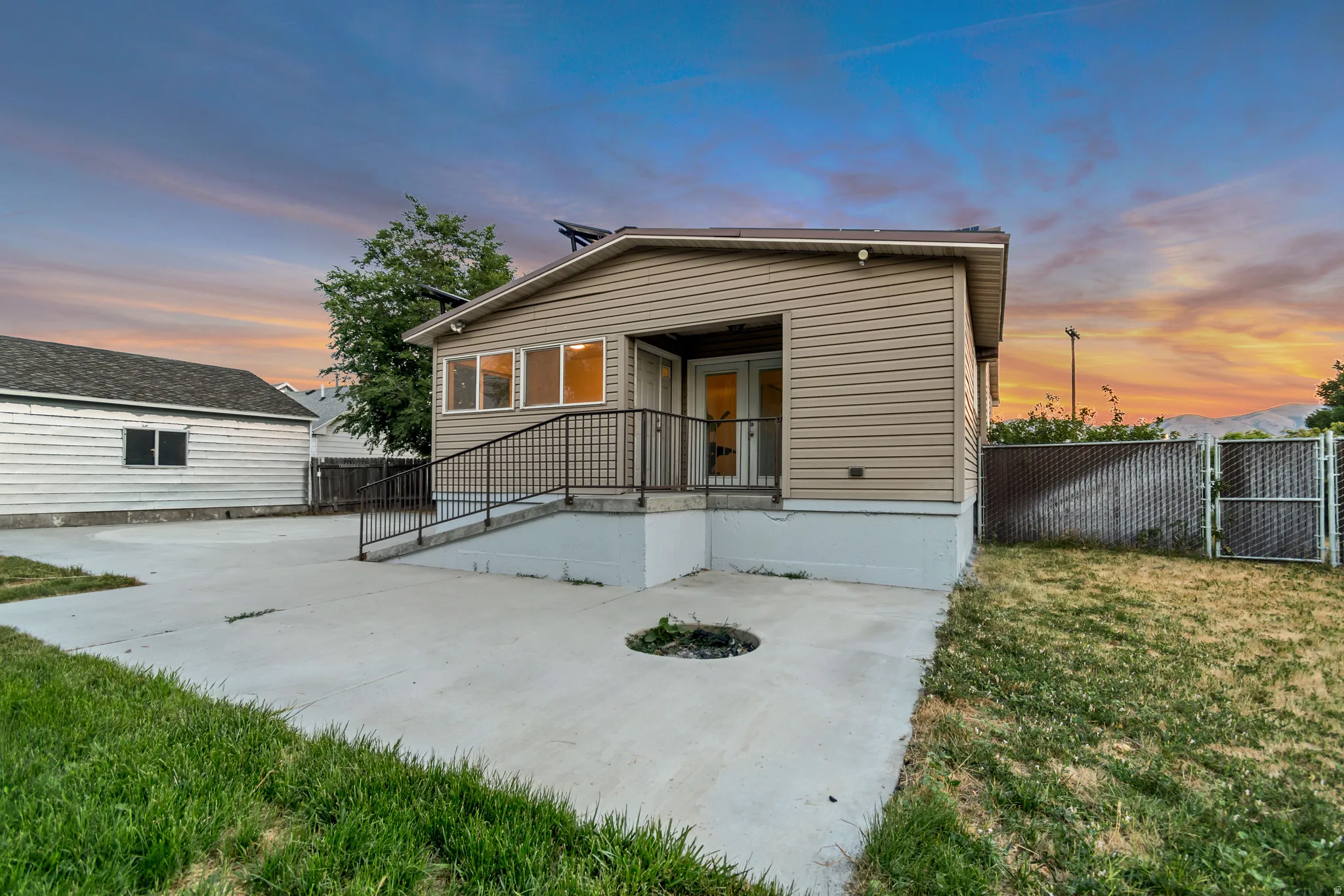 Contemporary-style residence with tan siding, a concrete patio, and a metal handrail entry