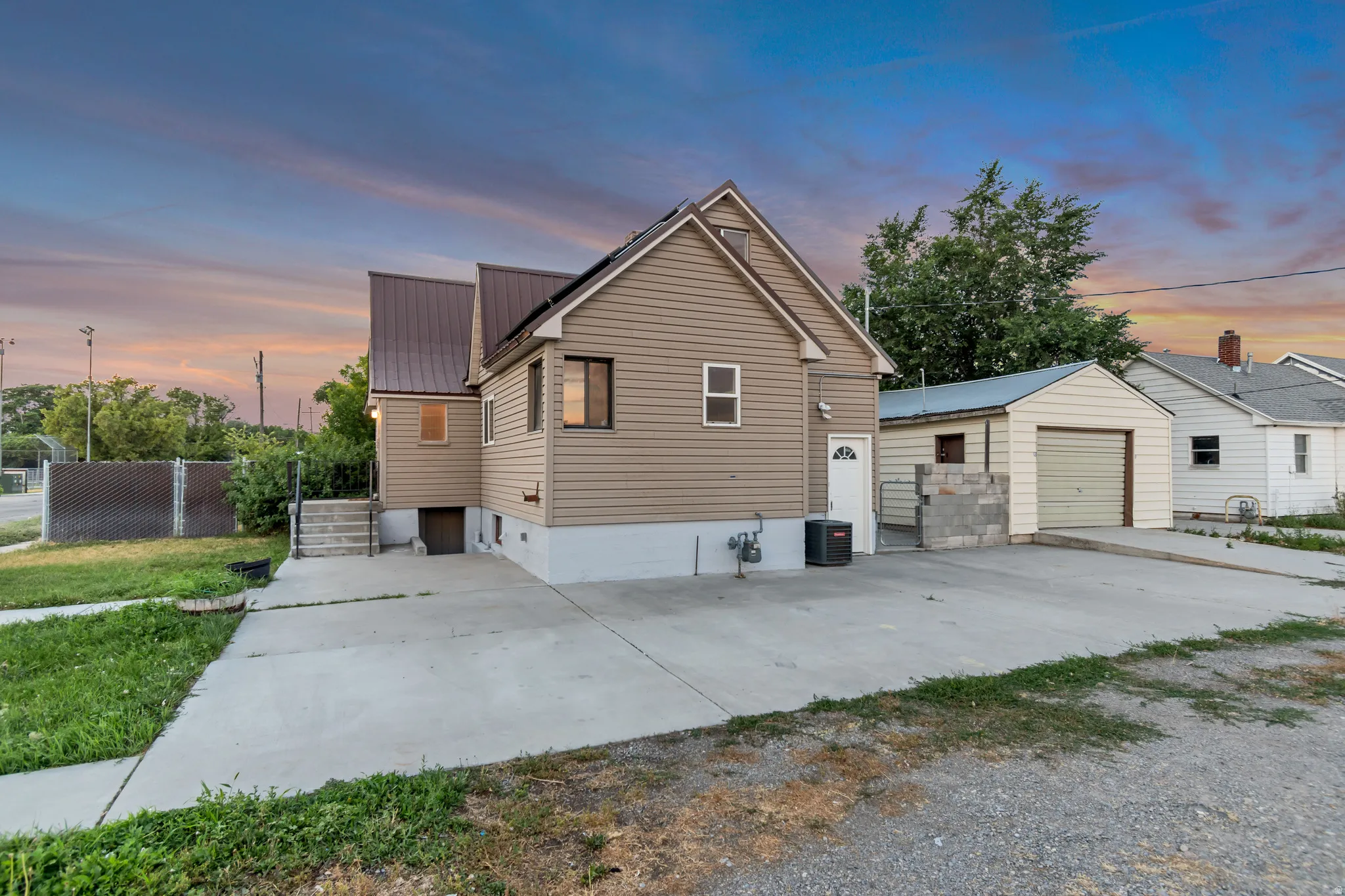 Rear exterior featuring tan siding, a brown metal roof, and a concrete driveway