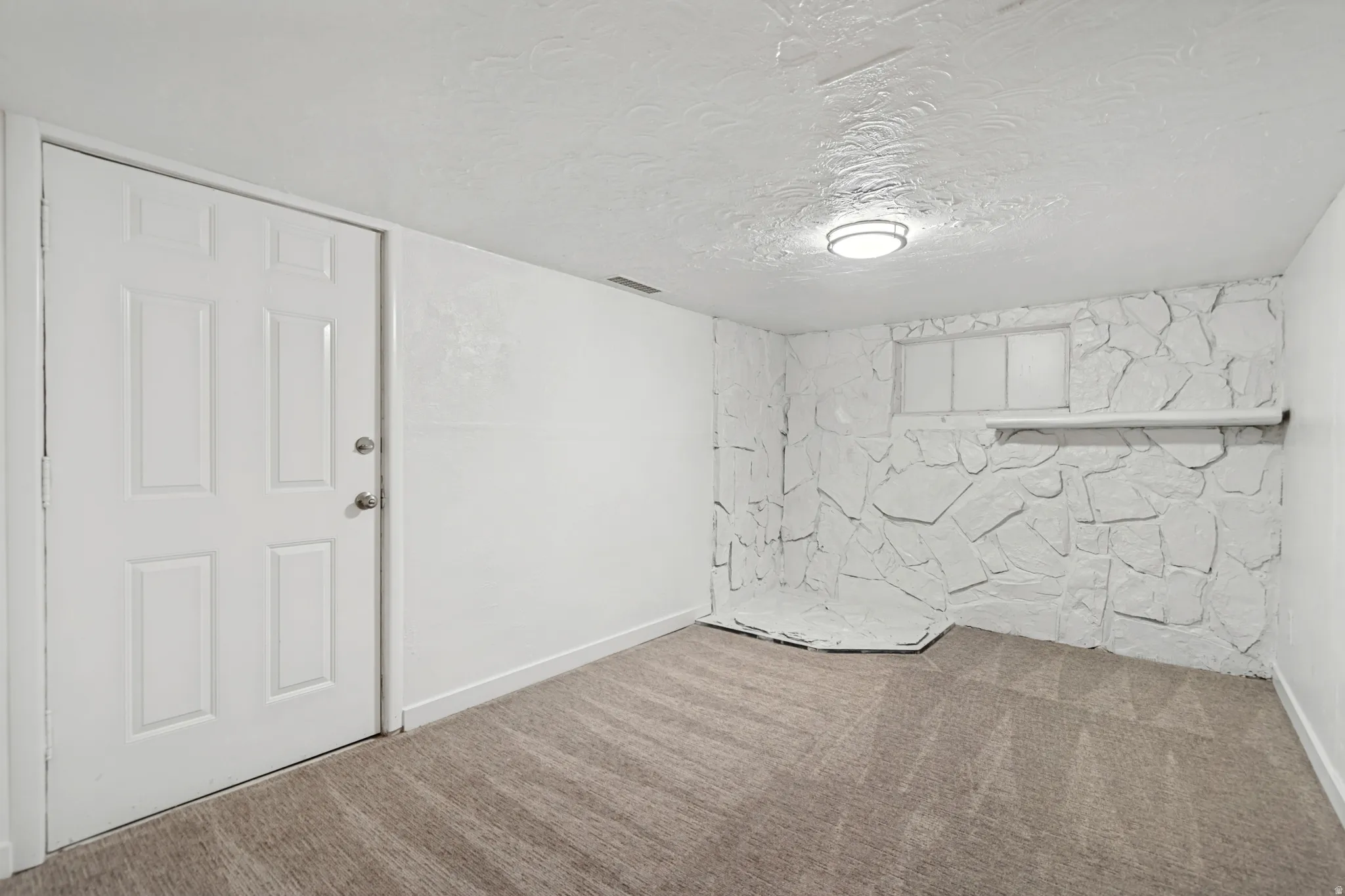 Carpeted room featuring a white interior door, white textured walls, and a recessed window with a white sill