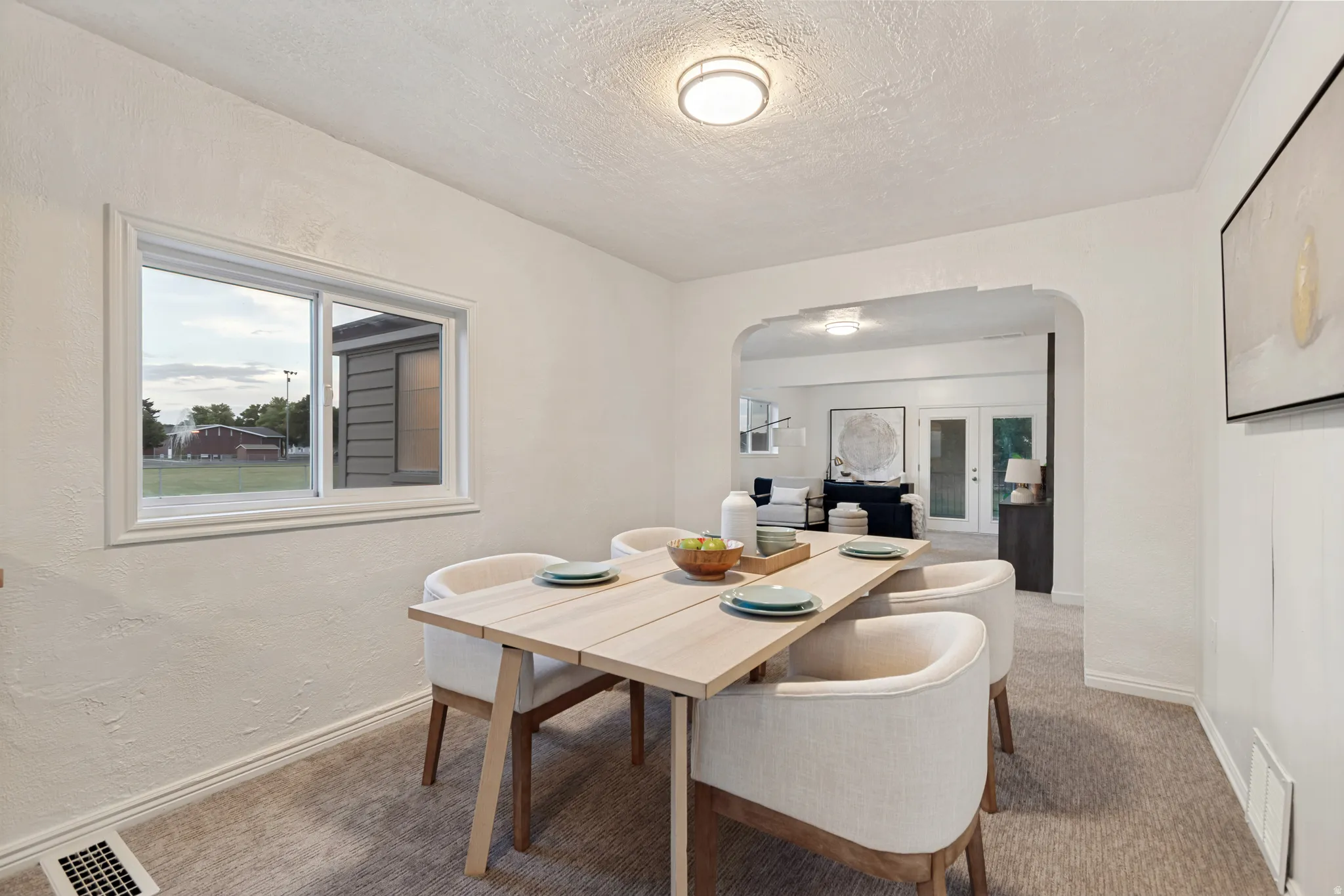 Bright dining area featuring a window with white trim, a decorative arched doorway, recessed lighting, white baseboards, and neutral-toned carpeting