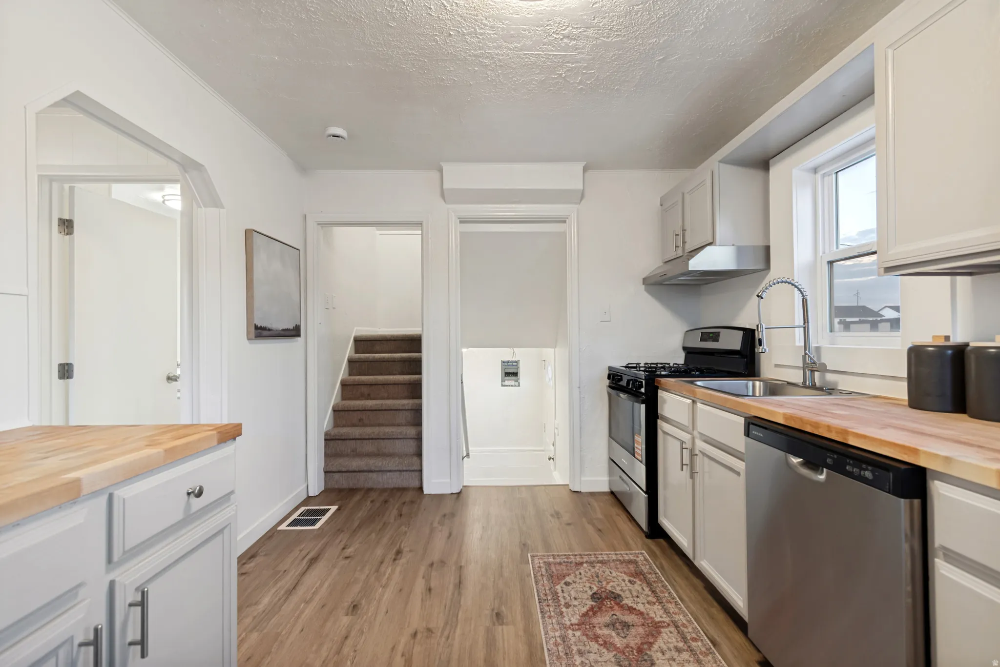 Kitchen featuring wood-finish flooring, light-toned cabinetry, wood countertops, stainless steel appliances, and a window above the sink