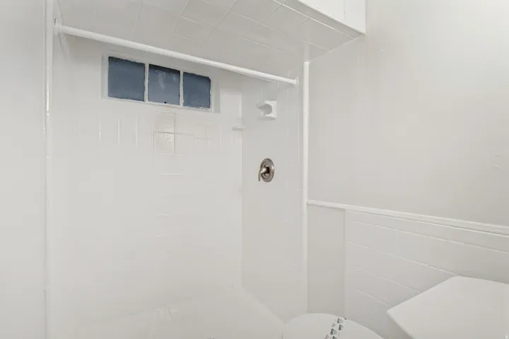 Bright white tiled shower enclosure featuring a satin nickel shower fixture, a privacy window, and a built-in shelf