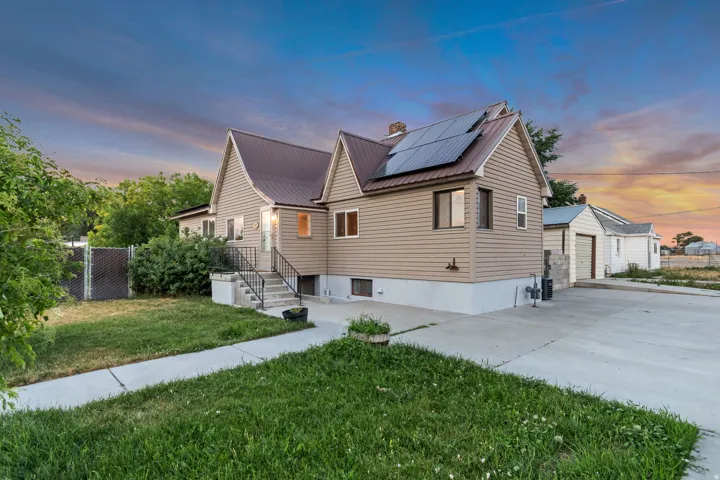Exterior featuring tan siding, a brown metal roof with solar panels, and a concrete driveway