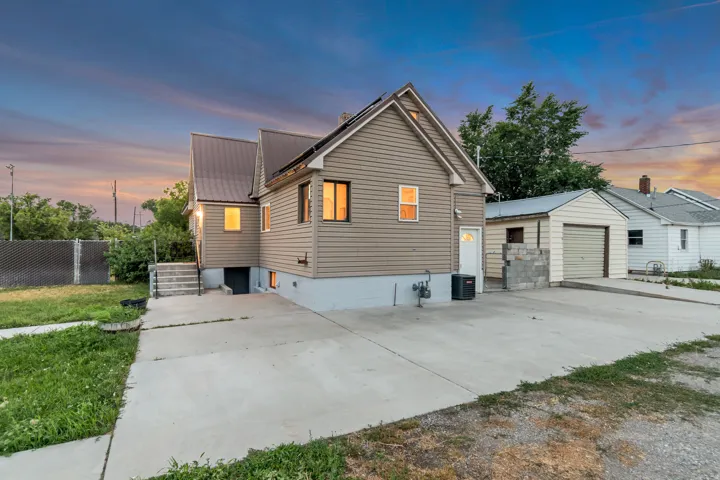Exterior featuring beige siding, a metal roof, multiple windows, a concrete driveway, and a detached garage