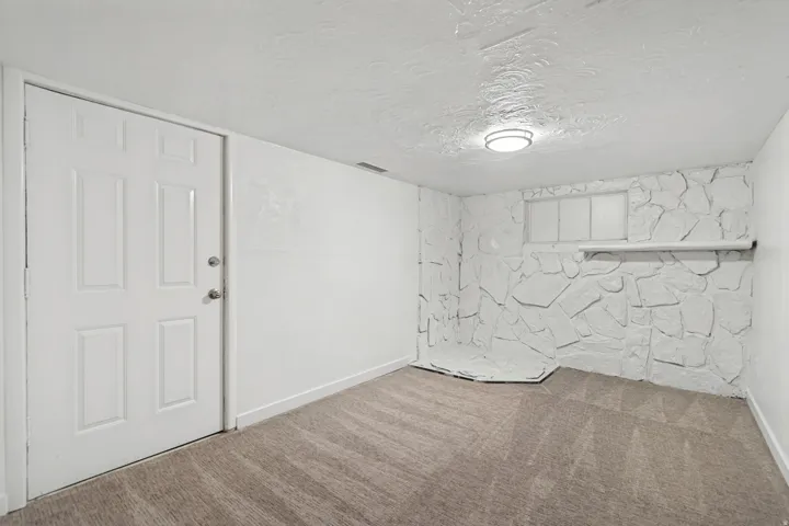 Carpeted room featuring a white interior door, white textured walls, and a recessed window with a white sill