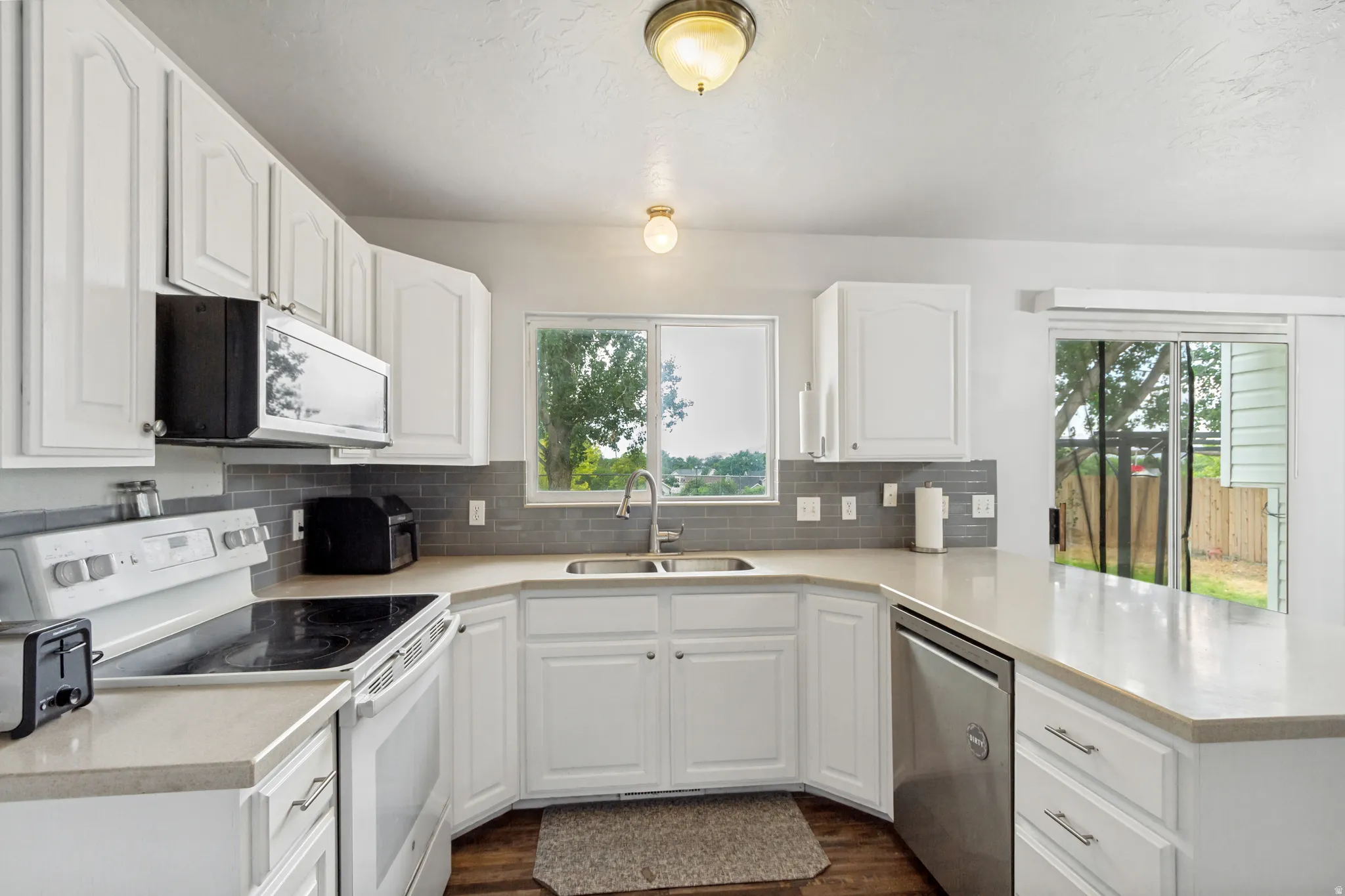 Modern kitchen featuring white cabinetry, light countertops, a tile backsplash, stainless steel dishwasher, and a built-in microwave