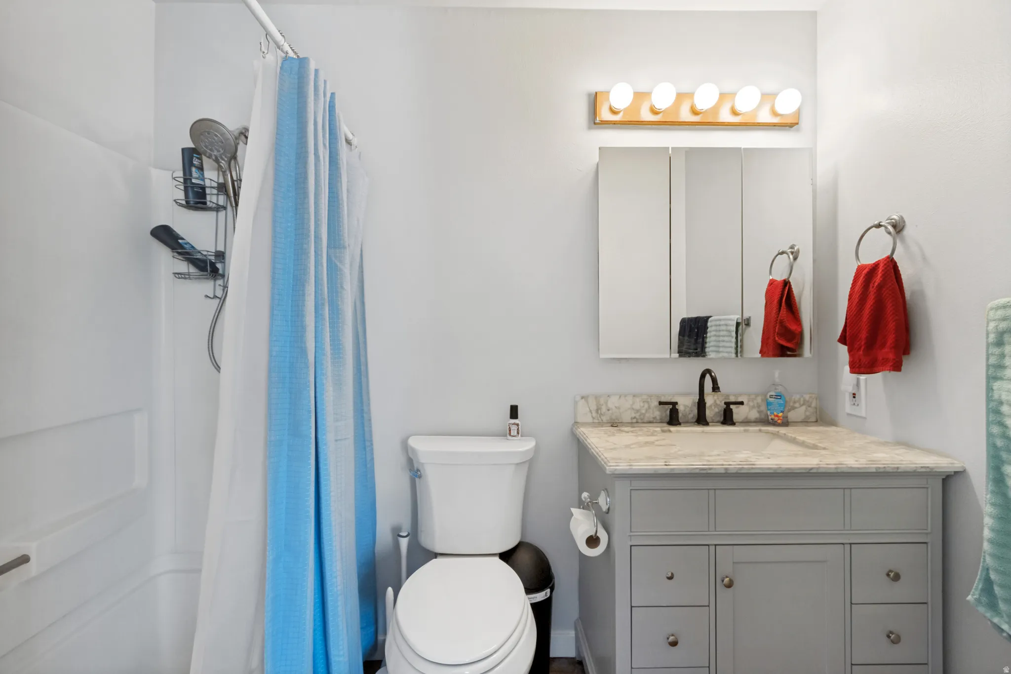 Bathroom featuring a white tub/shower combination, a vanity with a light-colored countertop, a gray base cabinet, a built-in medicine cabinet, and a five-light fixture