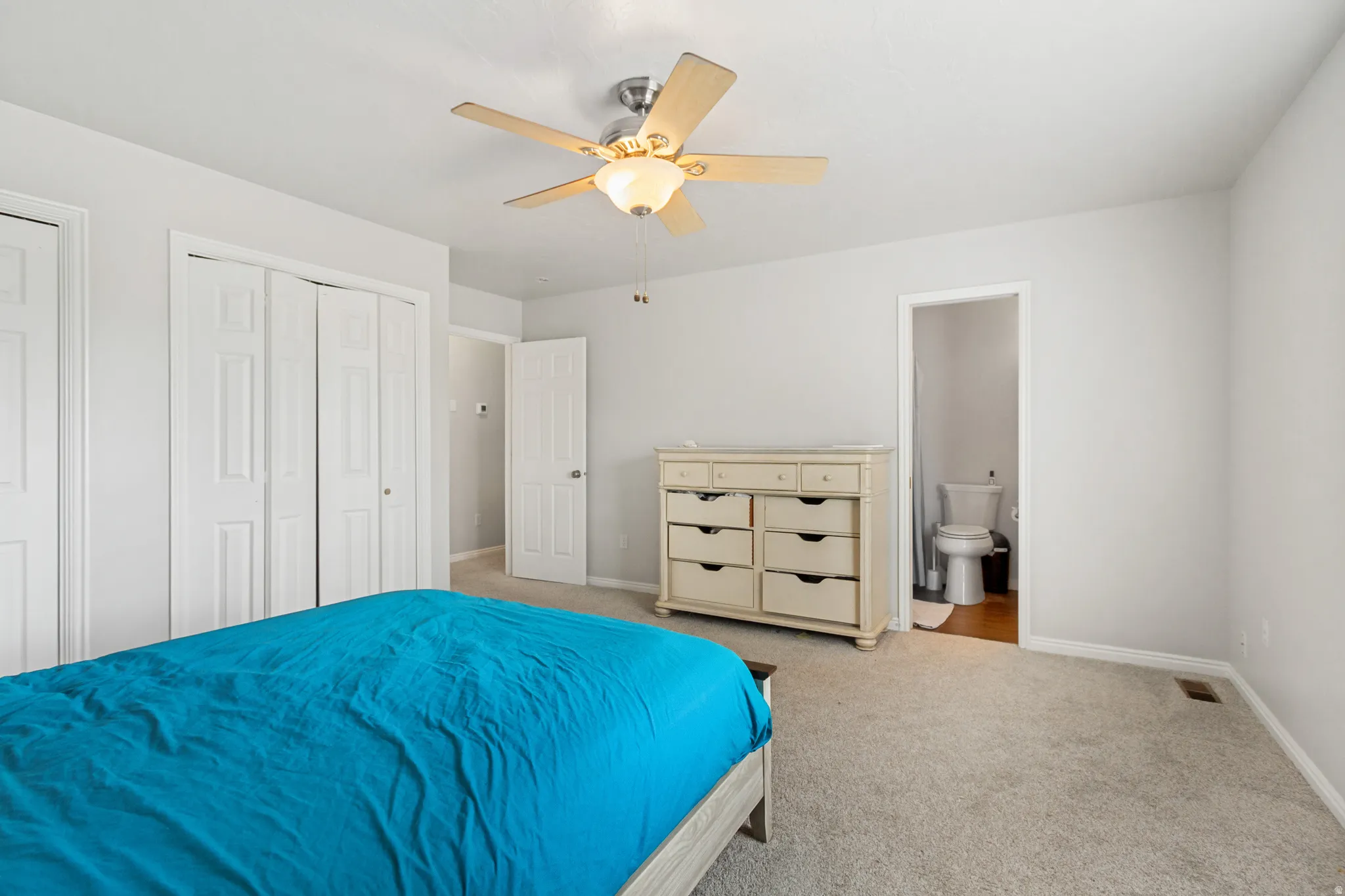 Neutral-toned bedroom featuring carpet flooring, a ceiling fan with light fixture, and two bi-fold closet doors