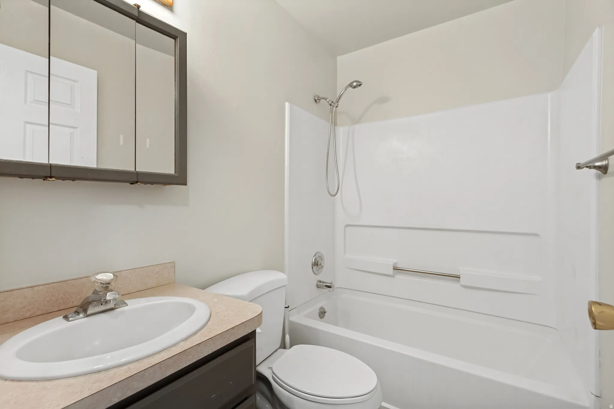 Bathroom featuring a vanity with an integrated sink, a medicine cabinet, a toilet, and a combined tub and shower unit with a white surround