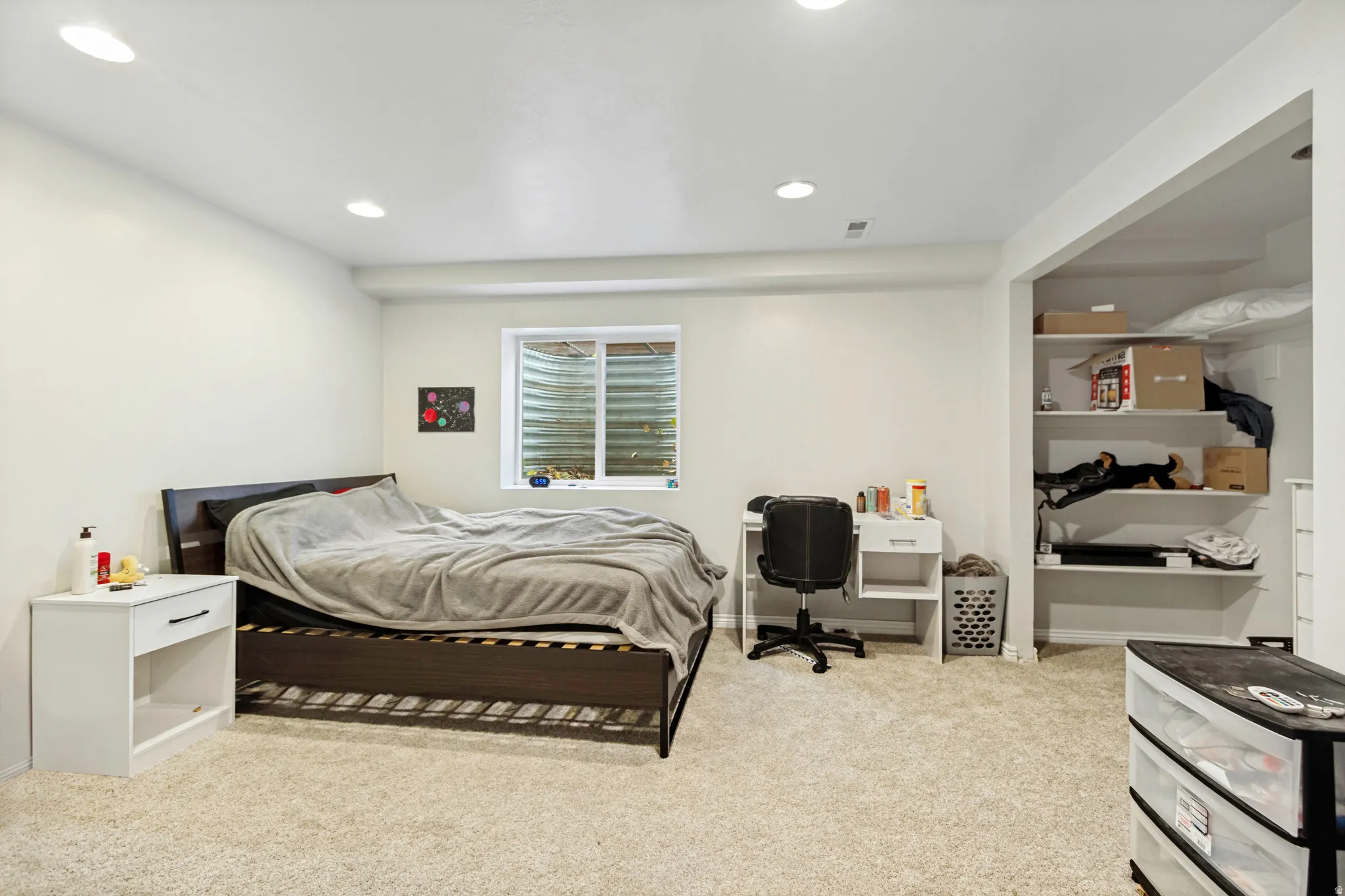 Carpeted room featuring a window with security grating, recessed lighting, and an open shelving unit