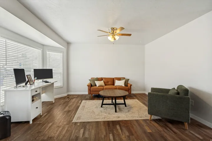 Bright interior space featuring wood-finish flooring, a bay window with blinds, and a ceiling fan with integrated lighting
