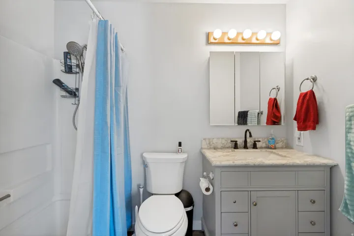 Bathroom featuring a white tub/shower combination, a vanity with a light-colored countertop, a gray base cabinet, a built-in medicine cabinet, and a five-light fixture