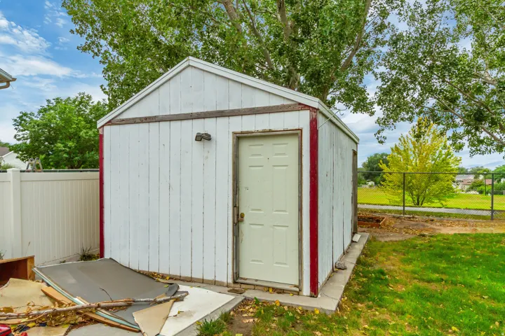Detached storage shed with white vertical paneling and a side-entry door, situated on a concrete slab
