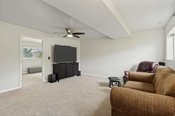 Carpeted recreation room featuring an overhead ceiling fan, white walls, and a window providing natural light