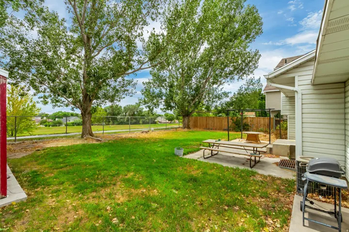 Expansive grassy yard with mature trees, a chain-link fence, and a concrete patio
