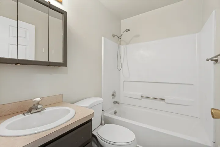Bathroom featuring a vanity with an integrated sink, a medicine cabinet, a toilet, and a combined tub and shower unit with a white surround
