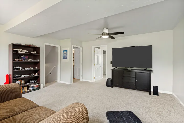 Spacious living area featuring neutral carpeting, light-toned walls, and a ceiling fan with integrated lighting