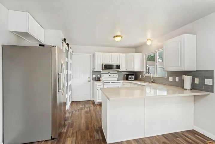 Kitchen featuring wood-finish flooring, white cabinetry, light-toned countertops, a subway tile backsplash, and a sliding barn door