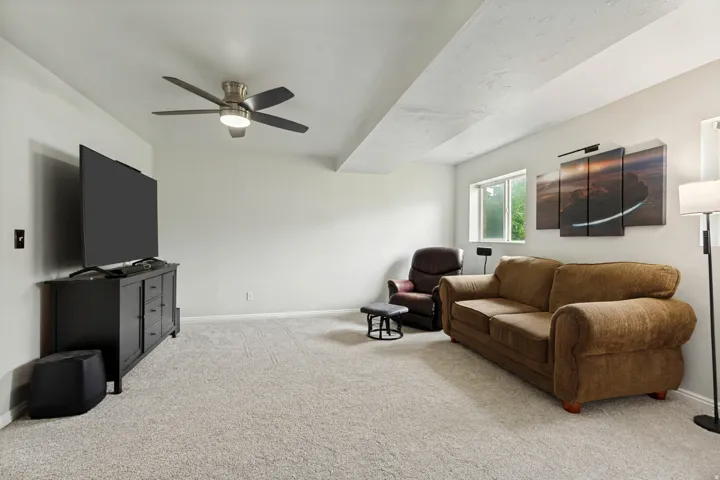 Carpeted room featuring a ceiling fan with integrated lighting, multiple windows, and a built-in media console
