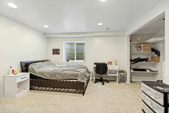Carpeted room featuring a window with security grating, recessed lighting, and an open shelving unit