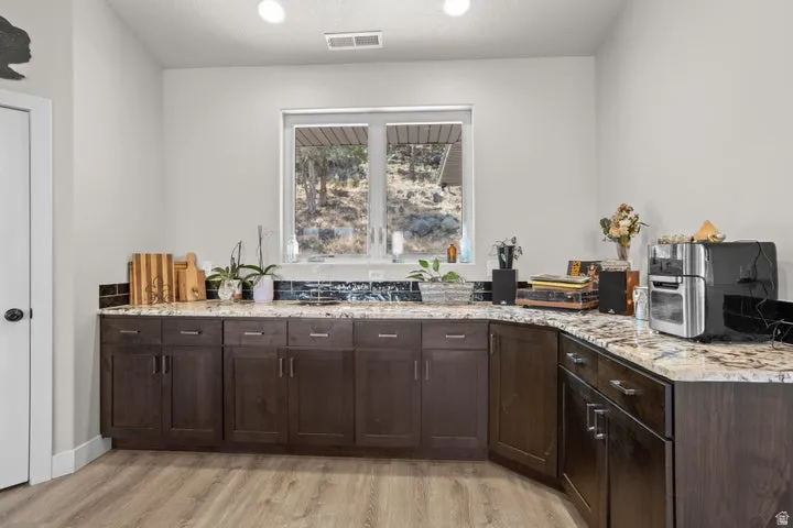 Kitchenette featuring dark wood cabinetry, light-toned stone countertops, a dark tile backsplash, and wood-finish flooring