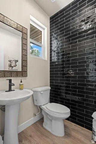 Contemporary powder room featuring a black subway tile accent wall, pedestal sink with matte black faucet, and wood-finish flooring