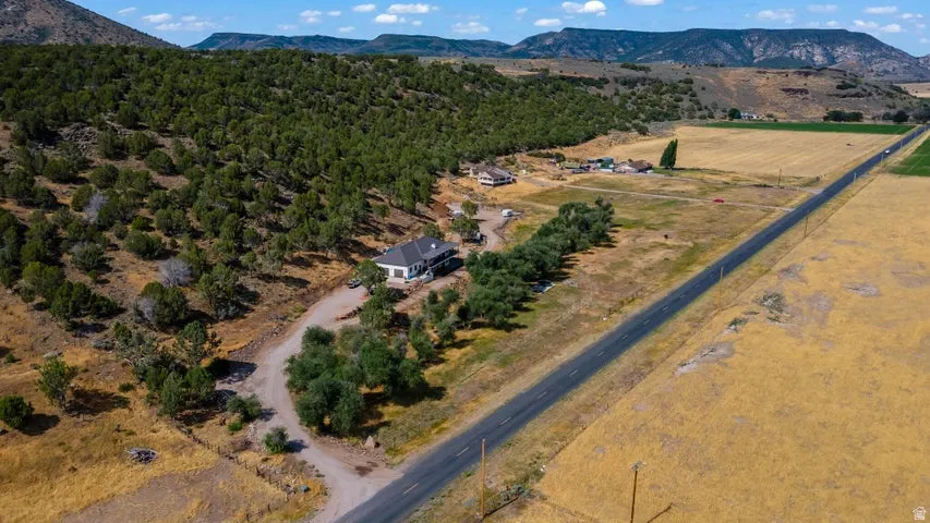 Expansive property featuring a main residence with a white exterior and dark roof, set against a backdrop of natural terrain with dense tree cover