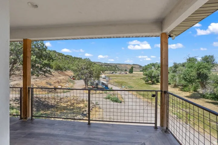 Covered balcony featuring wood-finish flooring, sturdy support pillars, and metal grid railing