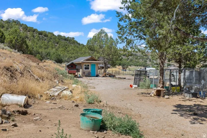 Rustic auxiliary structure with a vibrant blue entrance door, set against a backdrop of natural hillside landscaping and mature trees