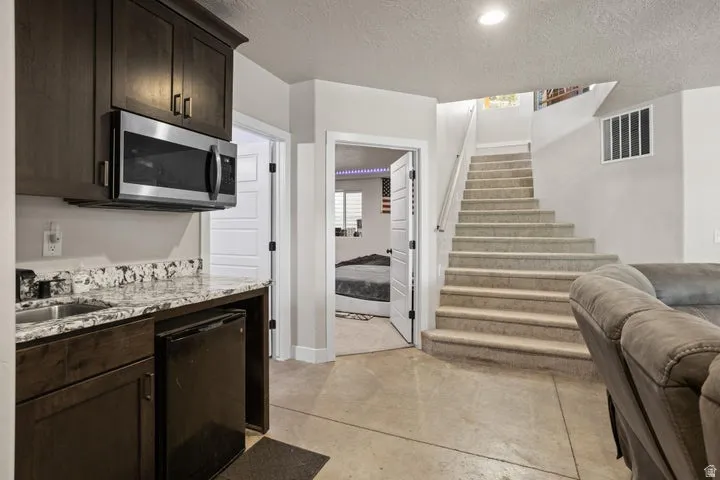 Built-in wet bar featuring dark wood cabinetry, a stainless steel microwave, and an undermount sink